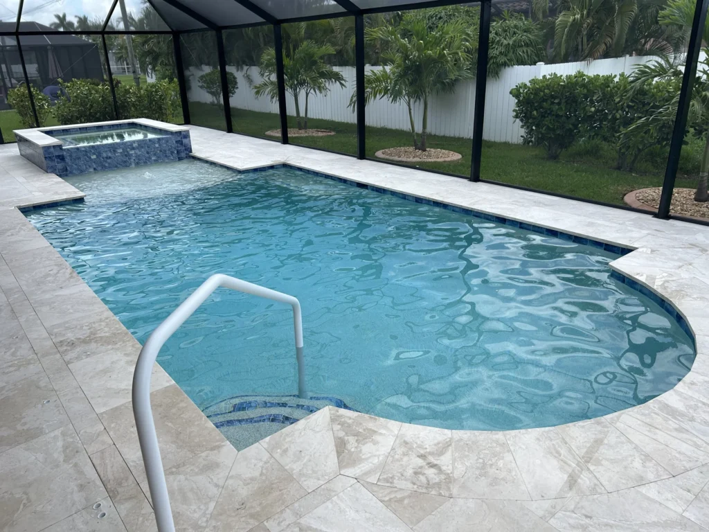 A freeform pool with a raised spa and travertine deck inside a screened lanai.