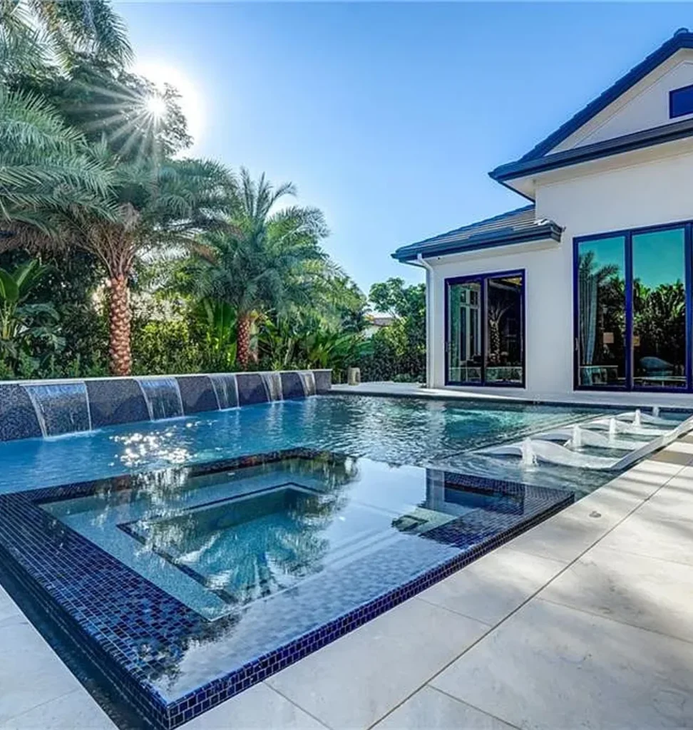 An elegant geometric pool with an all-glass-tile raised spa and a sheer descent waterfall wall beside a modern home.