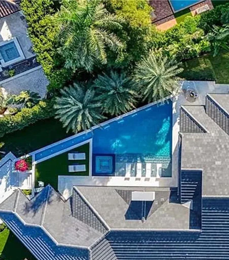 Aerial view of a modern rectangular pool with glass safety wall built into a rooftop terrace surrounded by palm trees.