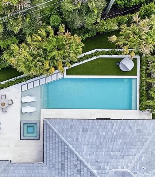 Aerial view of an L-shaped pool beside a modern home with a small separate plunge pool and loungers.