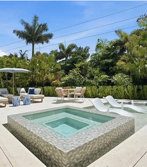 A tile-clad raised square spa dominates the foreground with a pool and loungers visible behind it.