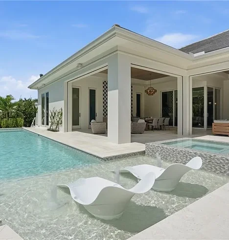 A modern home with a rectangular pool featuring a sun shelf with two lounge chairs and an attached raised spa.