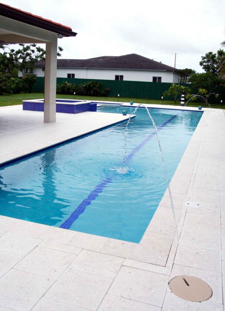 A long rectangular lap pool with a lane marker and deck jets, next to a raised blue-tiled spa under a covered patio.