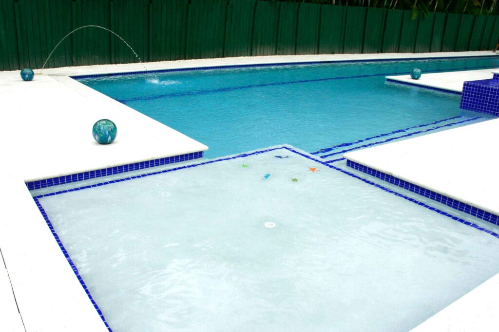 A shallow tiled splash ledge with sea-creature decals sits in front of a long lap pool with water arcing from decorative spheres.