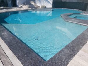 A geometric tile pool with a raised spa and sun shelf next to a wooden deck.