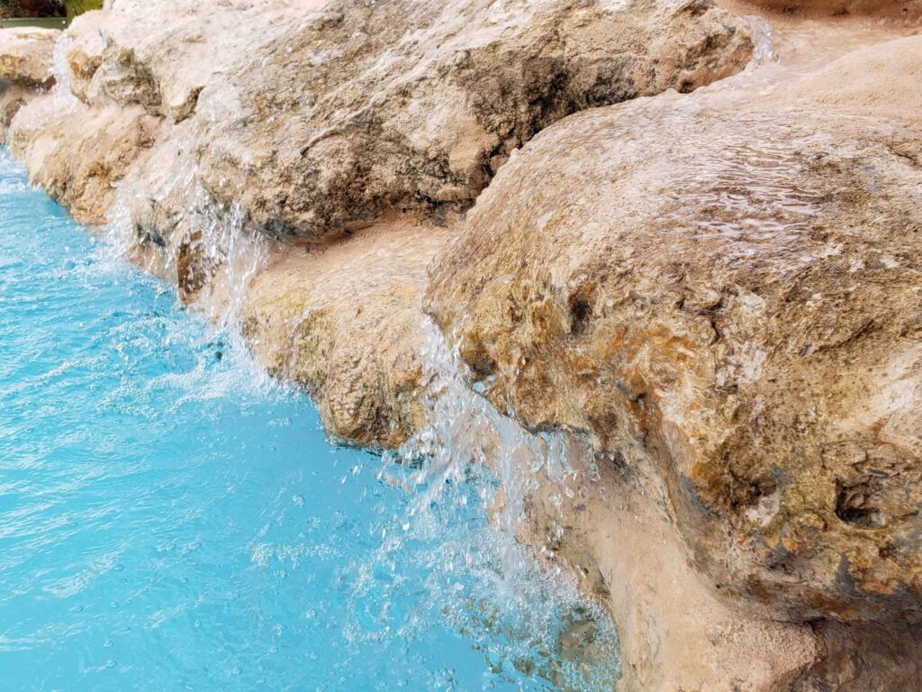 Close-up of water cascading over natural rock into a turquoise pool.