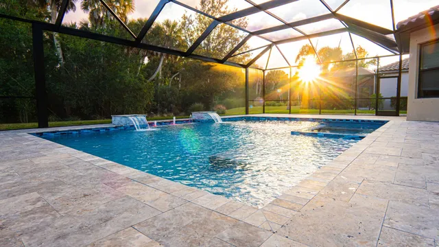 A screened rectangular pool with two water scuppers on a travertine paver patio at sunset.