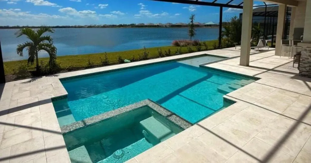 A rectangular pool with a raised spa and sun shelf overlooking a lake, enclosed by a screen structure.