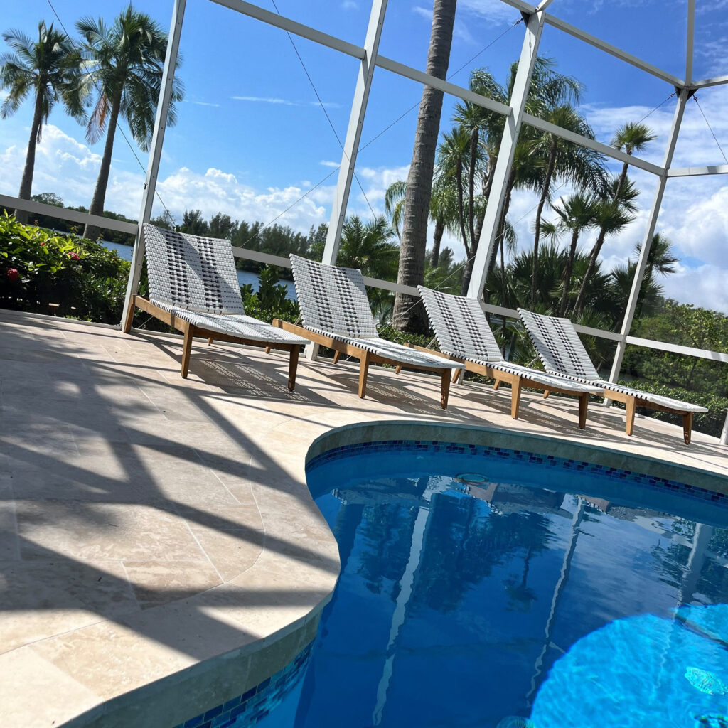 Four lounge chairs beside a curved pool edge under a screened enclosure with a waterfront palm view.
