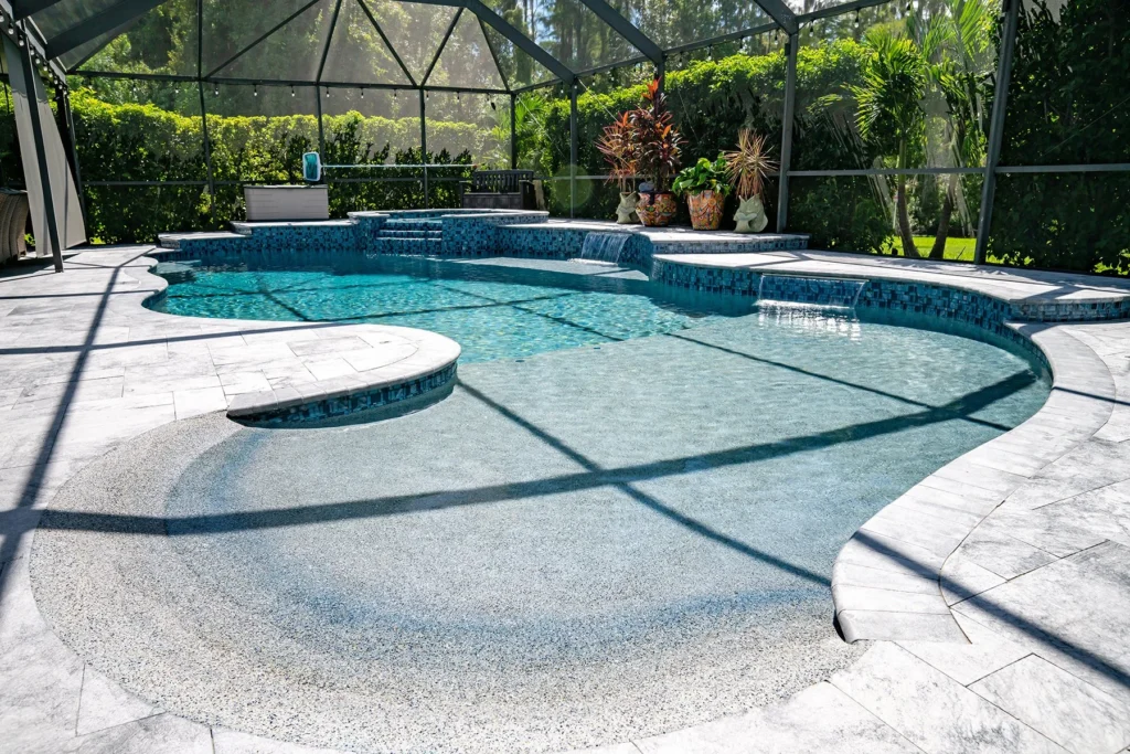 A freeform pool with a raised spa, spillover waterfall, and beach entry under a screened lanai.