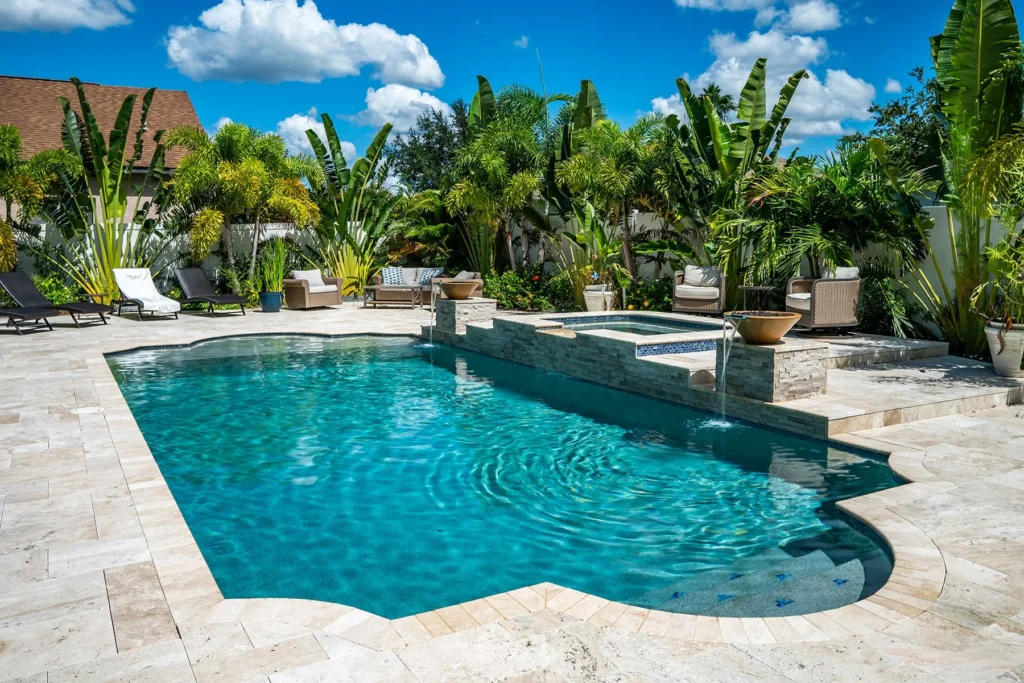 Freeform pool with raised stacked-stone spa and water bowl spillover surrounded by lush tropical landscaping on a travertine patio.