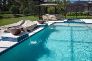 A rectangular pool with two bronze water bowls spilling into the water and a raised spa, under a screened enclosure.