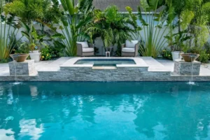 Rectangular backyard pool with a raised stacked-stone spa and two pouring water bowls, framed by tropical palms.