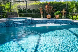 A blue mosaic-tiled freeform pool with a raised spa and small waterfall steps under a screened enclosure.