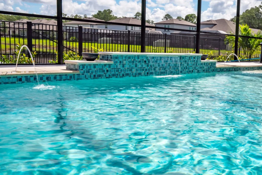 A tiled raised wall with a water feature spans between two sections of a screened pool.