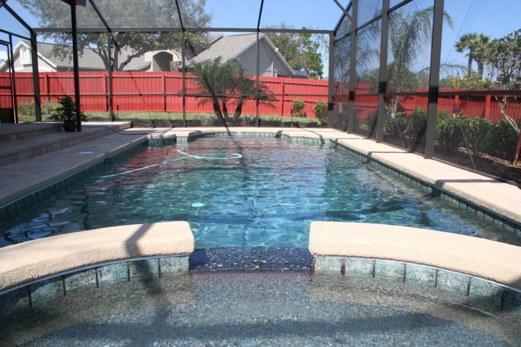 A raised spa with a tiled spillway pours into a rectangular pool under a screened enclosure.