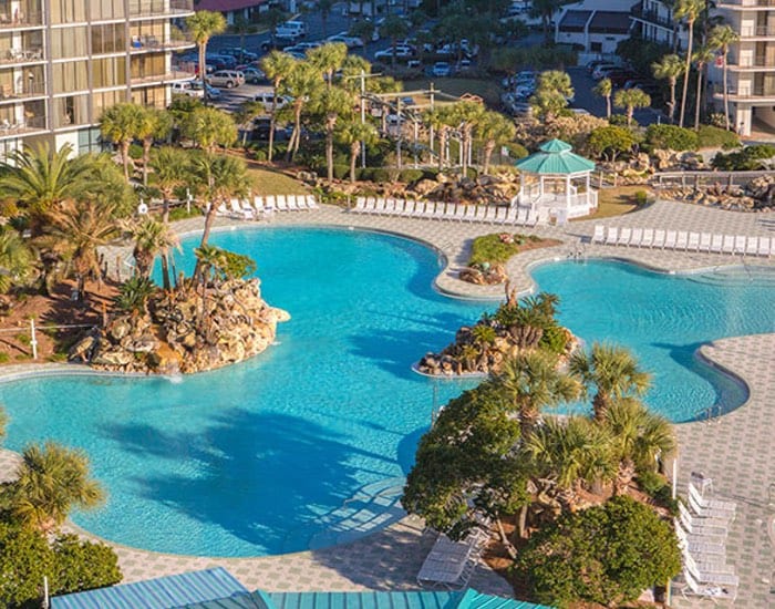 Aerial view of a large freeform resort pool with rock islands and waterfalls surrounded by palm trees and lounge chairs.