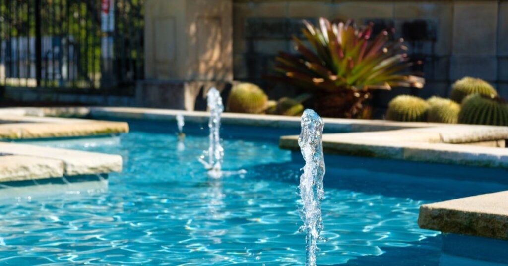 Close-up of bubbling water jets in a pool with stone coping and landscaped cactus garden in the background.
