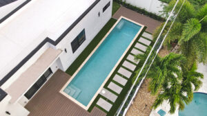 Aerial view of a narrow lap pool alongside a modern home with a stepping-pad walkway and turf.