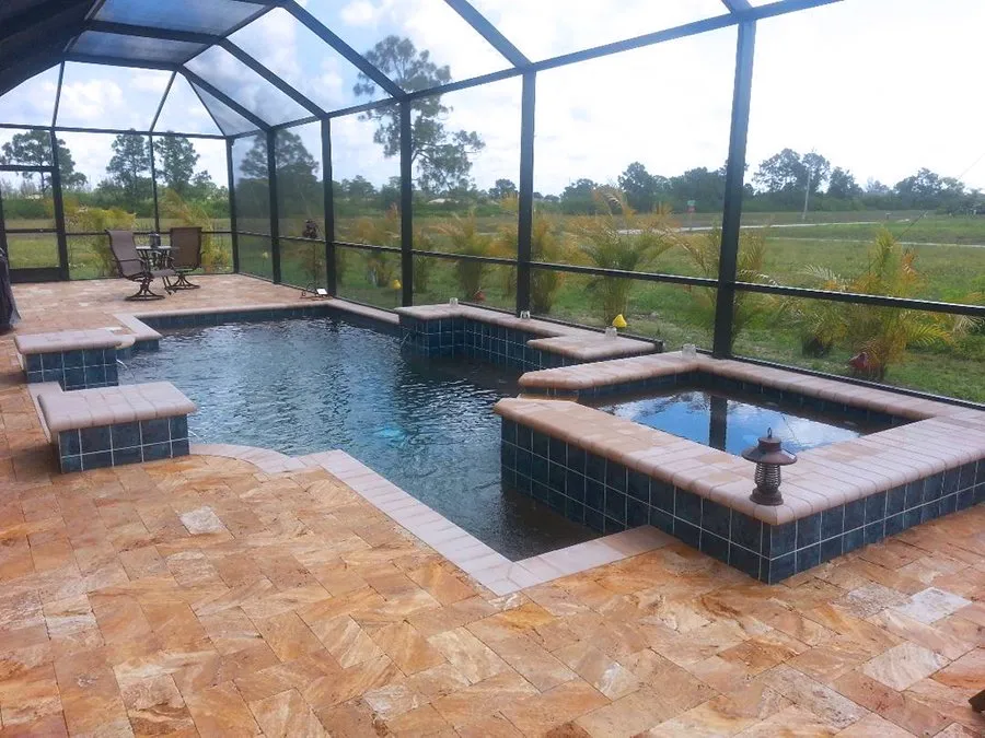 Freeform pool with raised tiled spa under a screened lanai and travertine deck overlooking an open field.