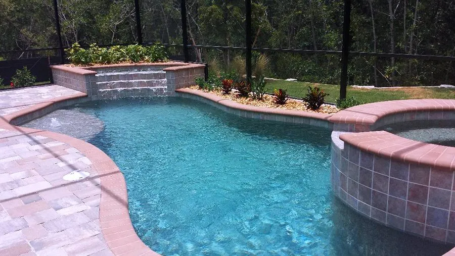 A freeform backyard pool with a raised spa and waterfall feature inside a screened enclosure.