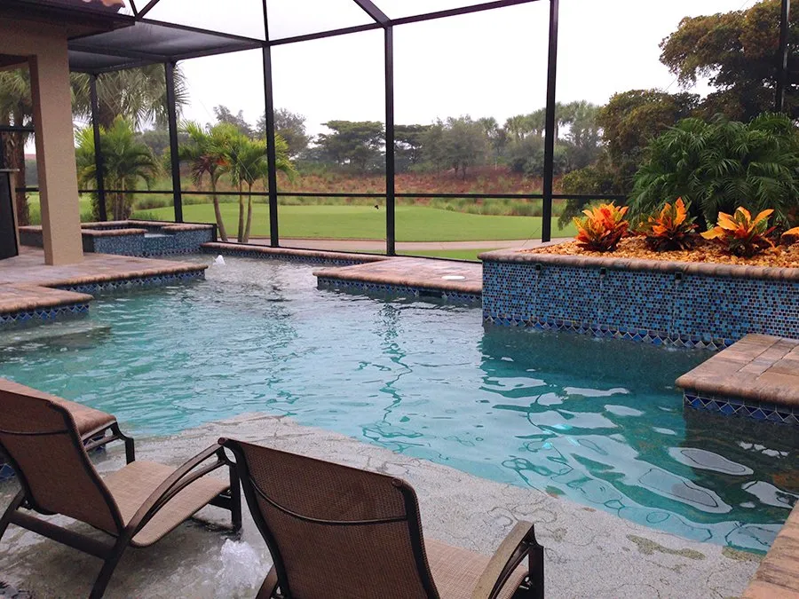 L-shaped pool with raised tiled spa under a screened enclosure overlooking a golf course.
