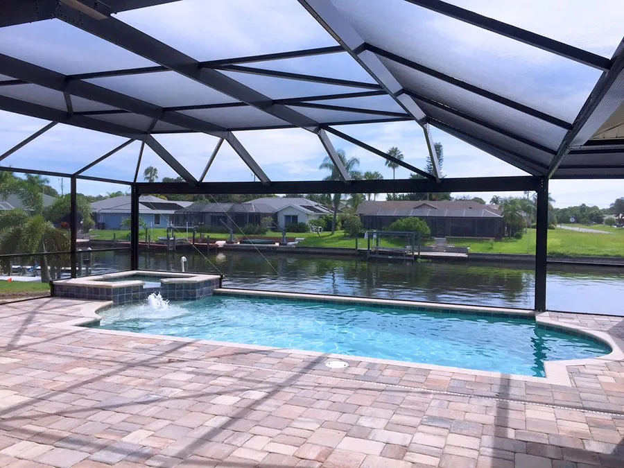 A screened lanai encloses a freeform pool with a raised spa spilling into it, overlooking a canal.