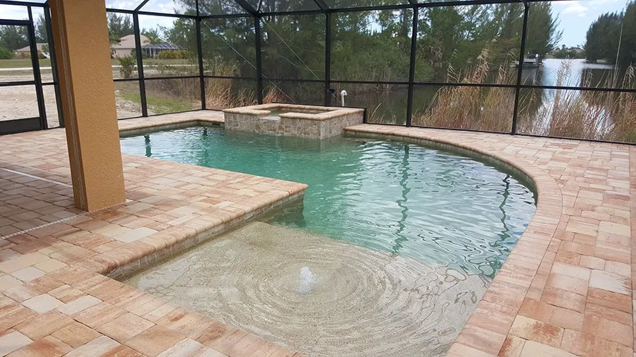 A freeform pool with a raised spa and shallow sun shelf under a screened lanai overlooking a canal.