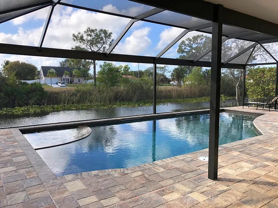 A rectangular screened pool overlooking a canal with houses across the water.