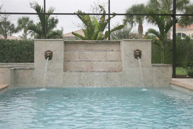 A raised travertine wall with two lion-head fountains spouting water into a pool under a screened enclosure.