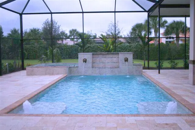 Rectangular pool under a screened enclosure with a raised spa and a stone waterfall wall with two spouts.