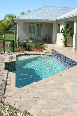 A small rectangular backyard pool with a raised spa and paver deck under open sky.