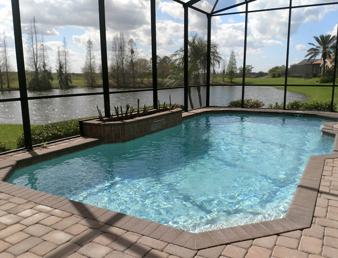 A screened geometric pool with a raised tiled wall overlooking a pond and golf course.