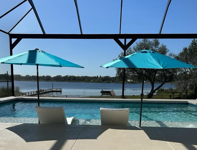 A small rectangular pool with in-water loungers under a screened enclosure overlooking a lake.