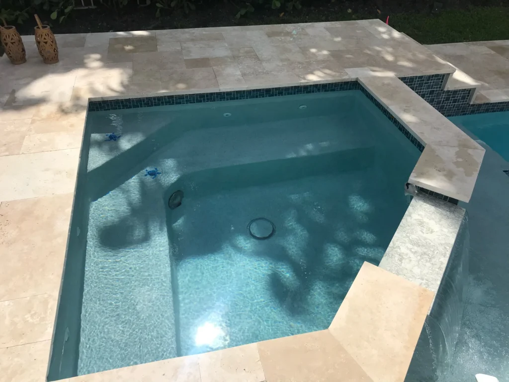 A raised spa with a tiled waterline and tanning step spills water into the adjacent pool.