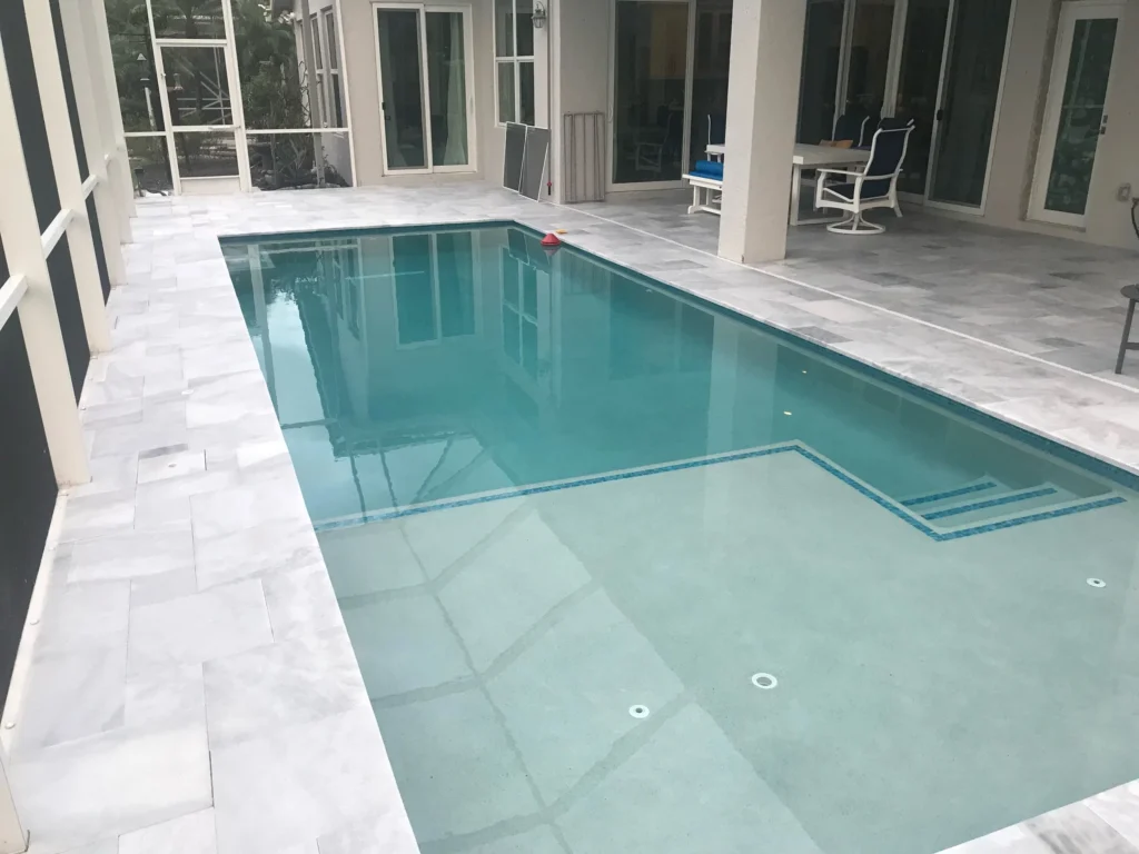 A rectangular backyard pool with a shallow tanning ledge under a screened patio enclosure.