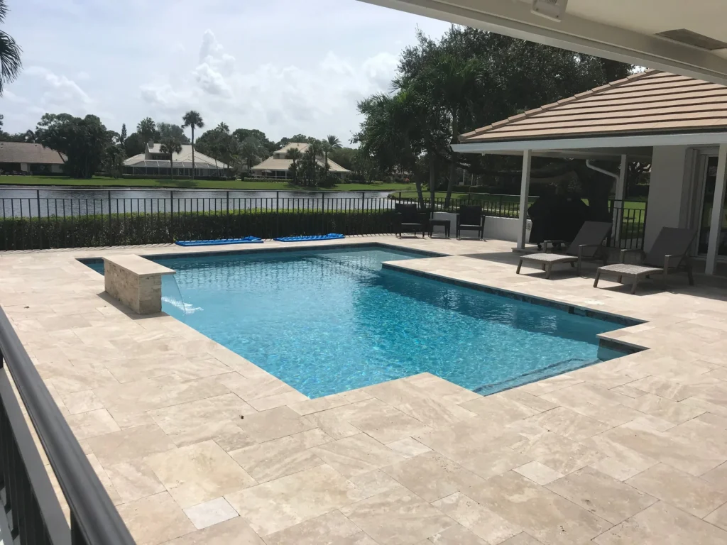 An L-shaped pool with a raised wall water feature overlooks a lake behind the home.