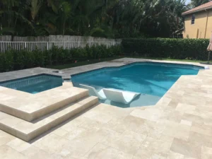 A geometric backyard pool with an attached raised spa and two in-pool loungers on a travertine paver patio.