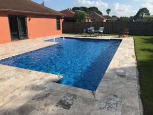 A rectangular backyard pool with travertine decking and two small deck jet fountains near the house.