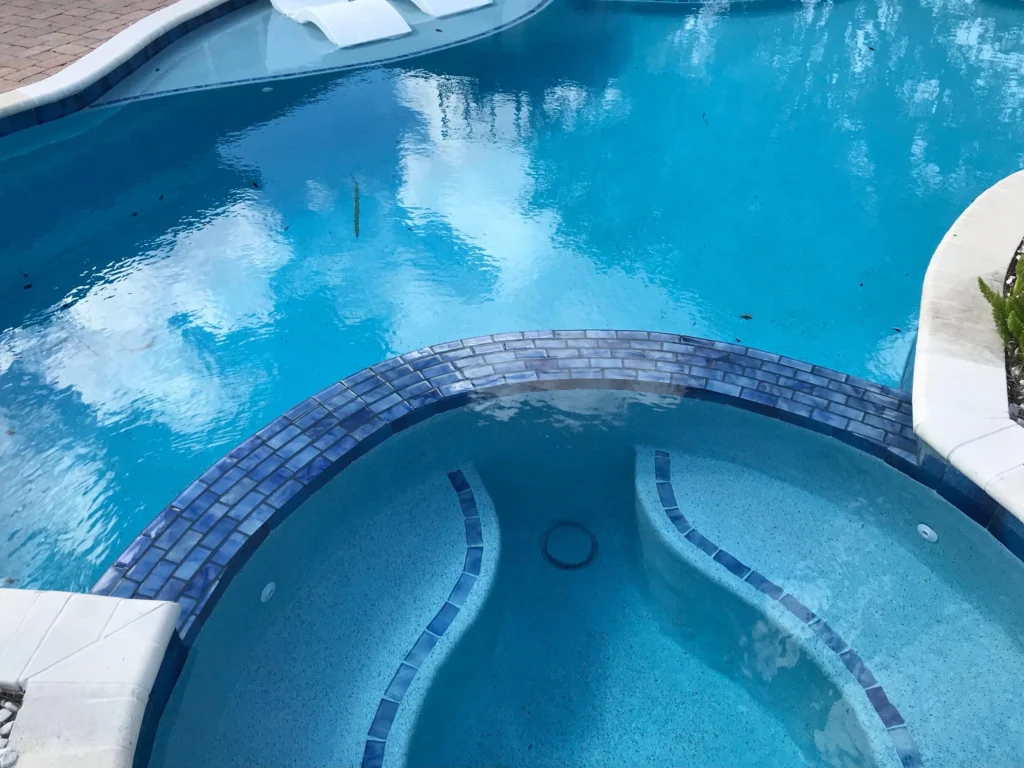 Close view of a round raised spa with decorative blue mosaic tile trim beside a freeform pool.