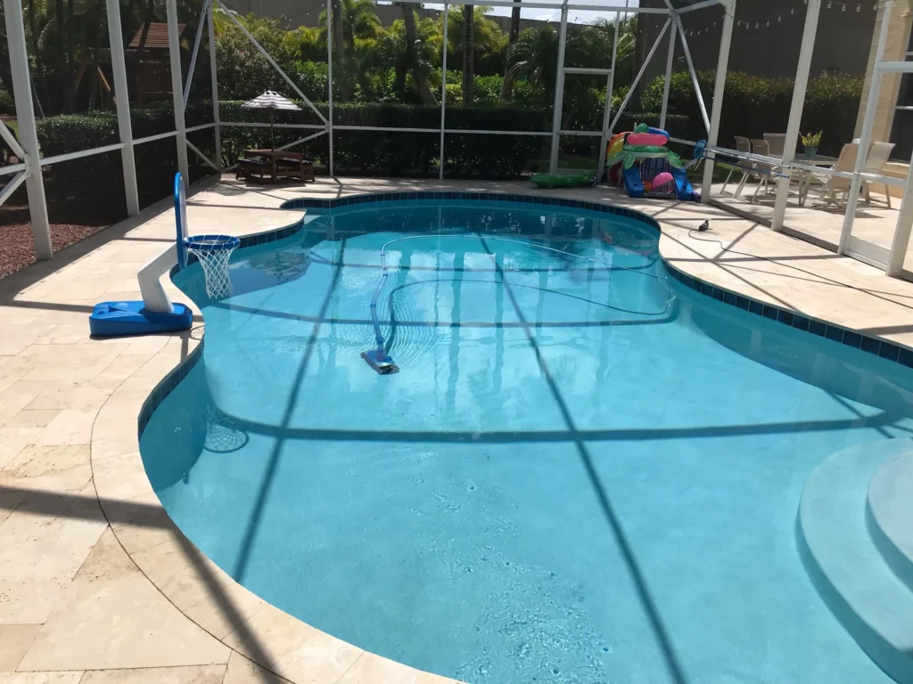 A freeform pool with a basketball hoop and pool cleaner inside a screened patio enclosure.