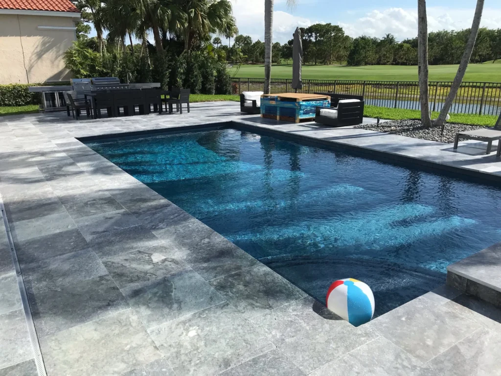 A rectangular pool with dark water and a travertine deck overlooking a golf course fairway.