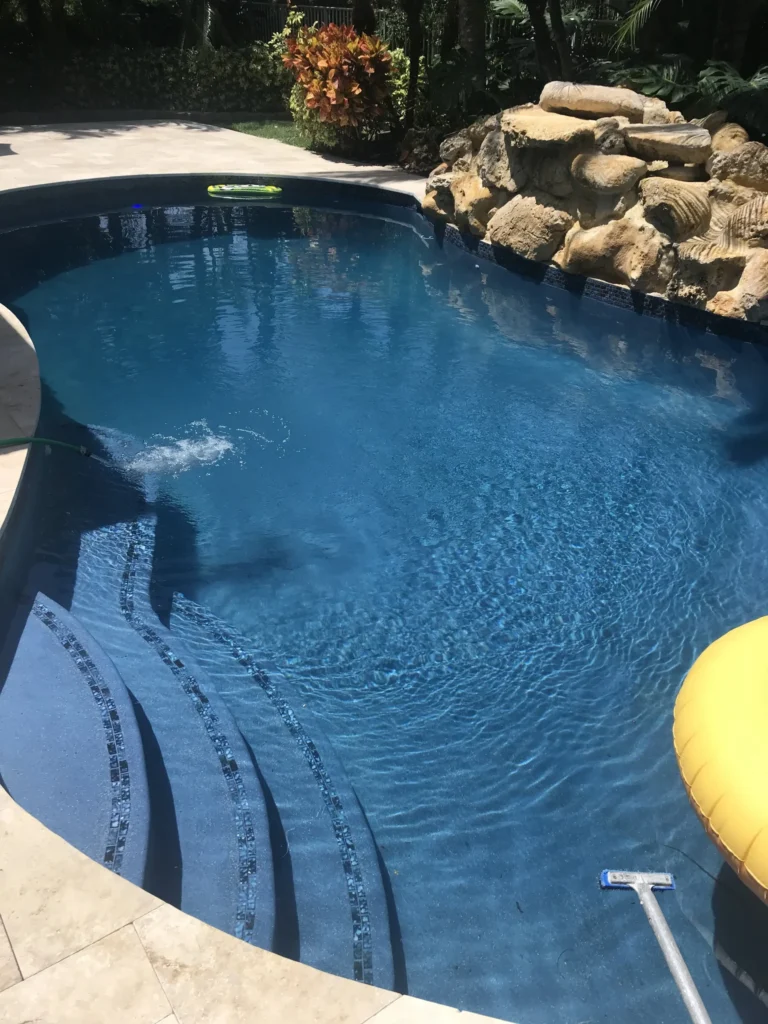 A freeform backyard pool with curved tiled steps and a natural stone waterfall feature.