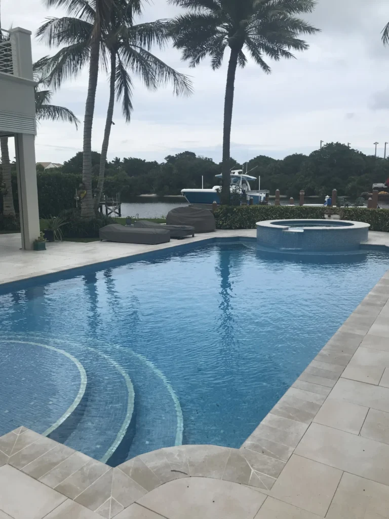 A freeform pool with a round tanning ledge and raised spa overlooking a canal with palm trees.