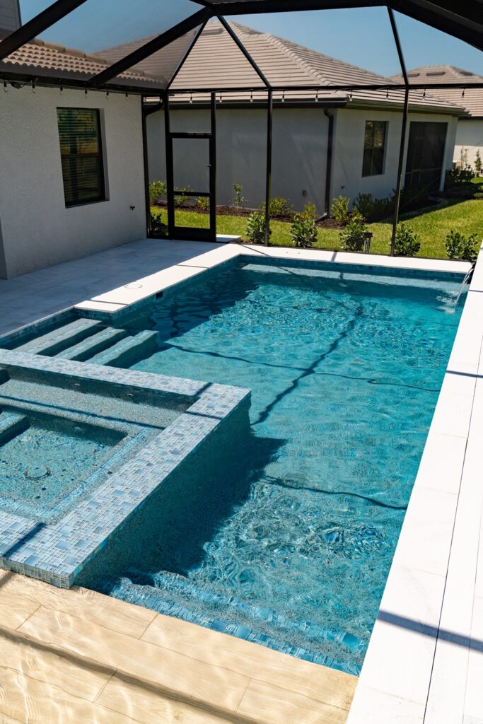 A rectangular pool with a raised elevated spa in a screened lanai next to a stucco home.