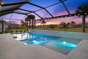 A multi-level pool and raised spa glow with blue LED lighting under a screened enclosure at dusk, with a stone accent wall and open field view beyond.