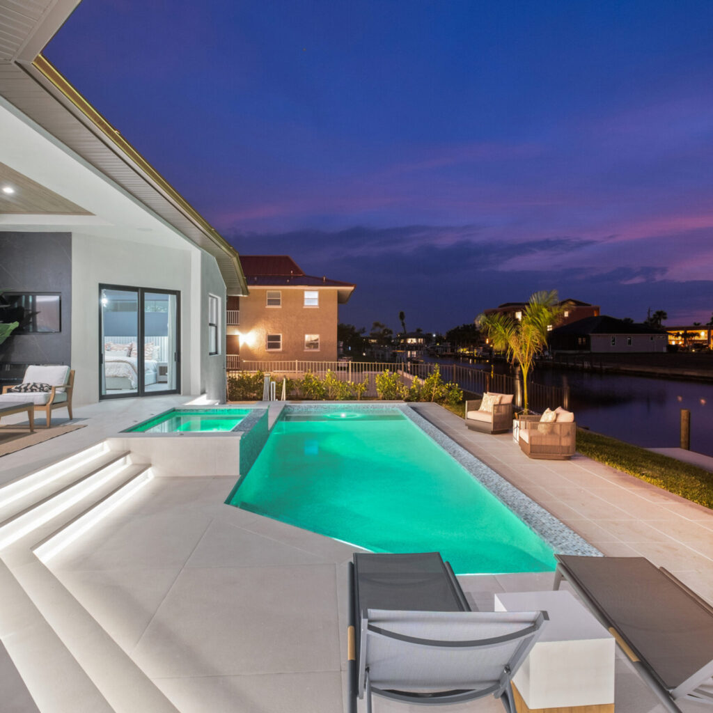 A modern rectangular pool with raised spa glowing turquoise at dusk beside a canal.