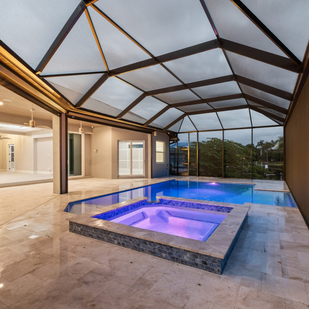 A screened lanai with a raised tiled spa lit purple beside a rectangular pool at dusk, overlooking a canal.