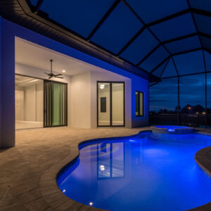 A freeform pool with blue LED lighting and a raised spa under a screened enclosure at night.