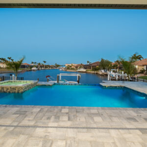 An infinity-edge pool and raised spa overlook a canal lined with docked boats at dusk.